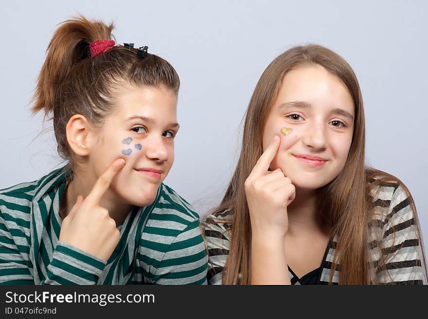 Two beautiful smiling teenage girls showing hearts on their faces.