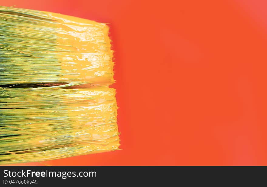 Tip of a paint brush with yellow paint and a orange canvas with copy space in the background. Tip of a paint brush with yellow paint and a orange canvas with copy space in the background