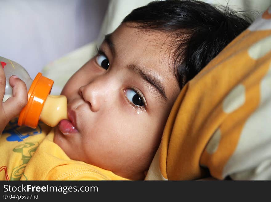 A crying young boy drinking milk from a bottle. A crying young boy drinking milk from a bottle