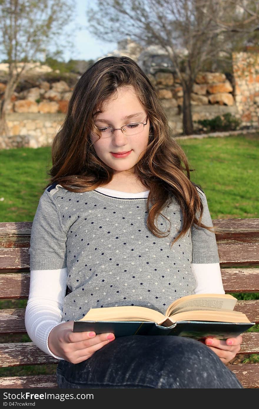 Young girl with glasses, sitting in the park and reading a book. Young girl with glasses, sitting in the park and reading a book