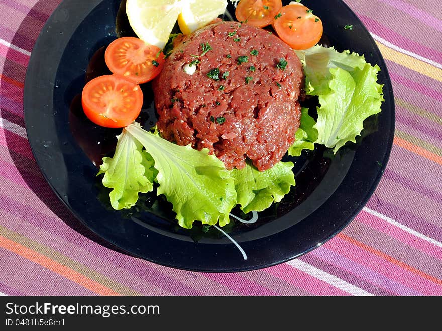 Raw ground beef with vegetables on a black dish