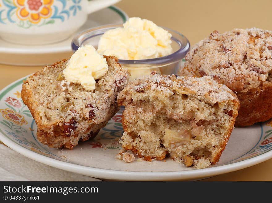 Two nut muffins, one cut in half with butter, on a plate. Two nut muffins, one cut in half with butter, on a plate