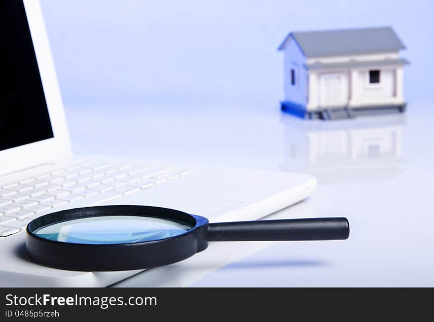 Black magnifying glass on laptop and a model house. Black magnifying glass on laptop and a model house