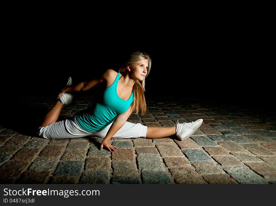 Beautiful blonde girl training at night on old pavement made of old stone tiles. Picture with black copy space. Beautiful blonde girl training at night on old pavement made of old stone tiles. Picture with black copy space.