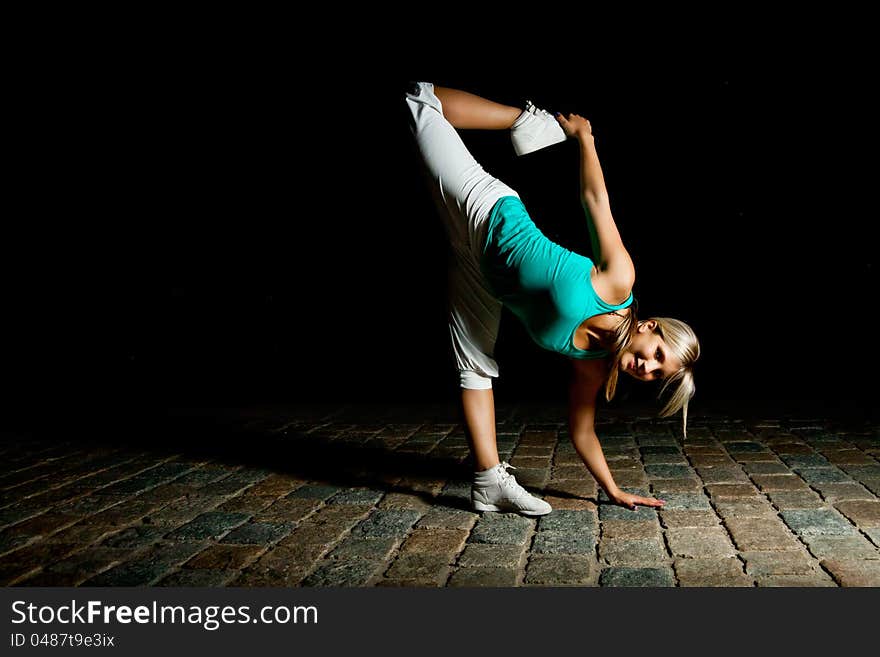 Beautiful blonde girl training at night on old pavement made of old stone tiles. Picture with black copy space. Beautiful blonde girl training at night on old pavement made of old stone tiles. Picture with black copy space.