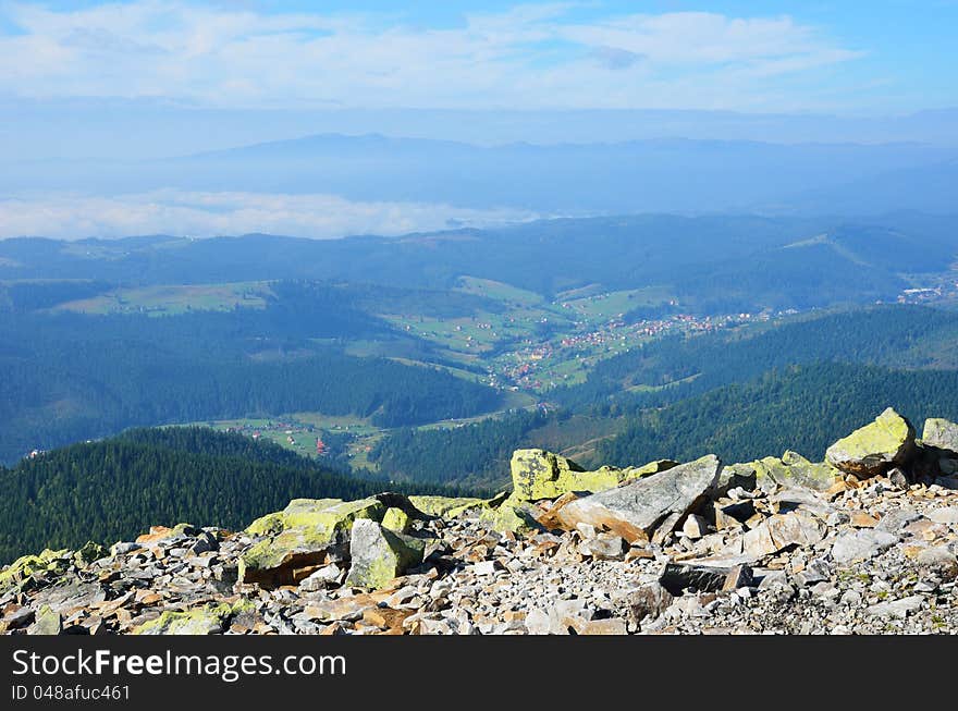 Carpathians are photographed on the peak. There are forested mountains, gently sloping hills, broad poloninas and green valley in the haze. In the foreground there is a stony slope. Carpathians are photographed on the peak. There are forested mountains, gently sloping hills, broad poloninas and green valley in the haze. In the foreground there is a stony slope.