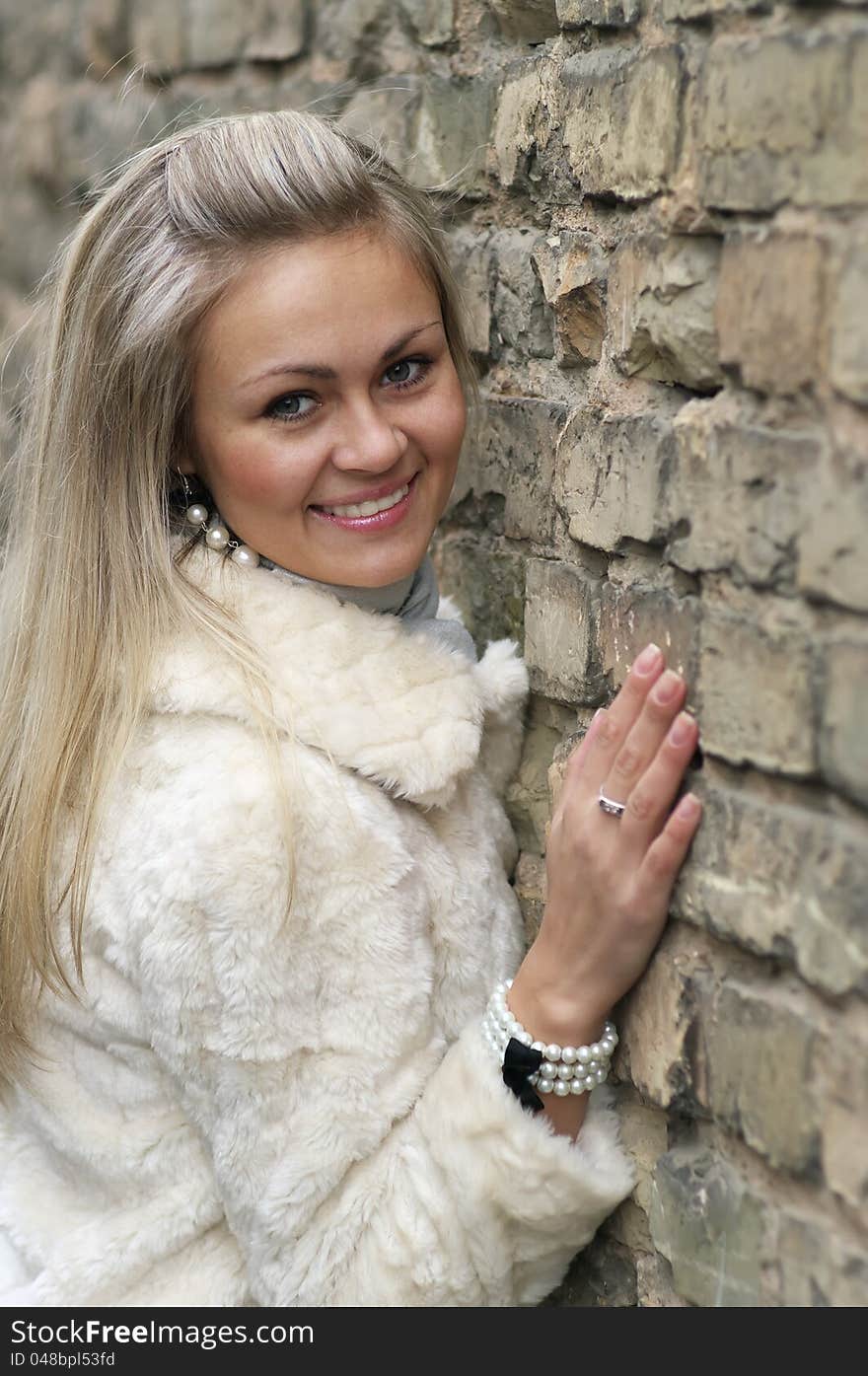 Young Happy Woman In Fur Coat Near an Old Brick Wall. Young Happy Woman In Fur Coat Near an Old Brick Wall