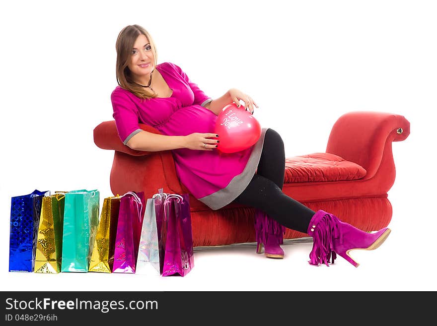 Pregnant woman in pink color dresses, with shopping bags on white background and sofa. Pregnant woman in pink color dresses, with shopping bags on white background and sofa