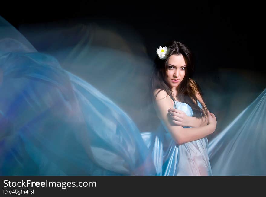 Beautiful girl in the blue dress from flying fabric on a black background