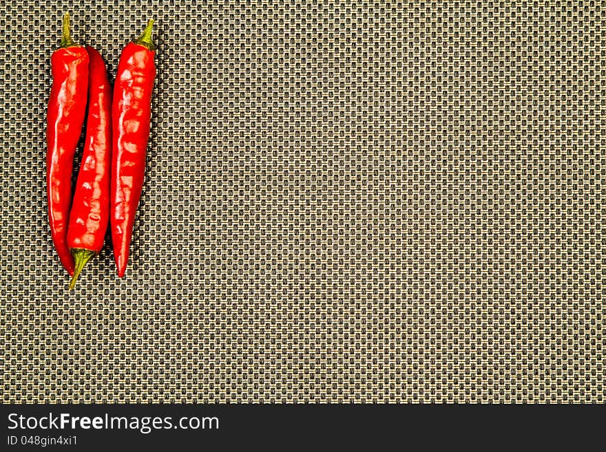 Three red hot peppers on a beige and black background. Three red hot peppers on a beige and black background