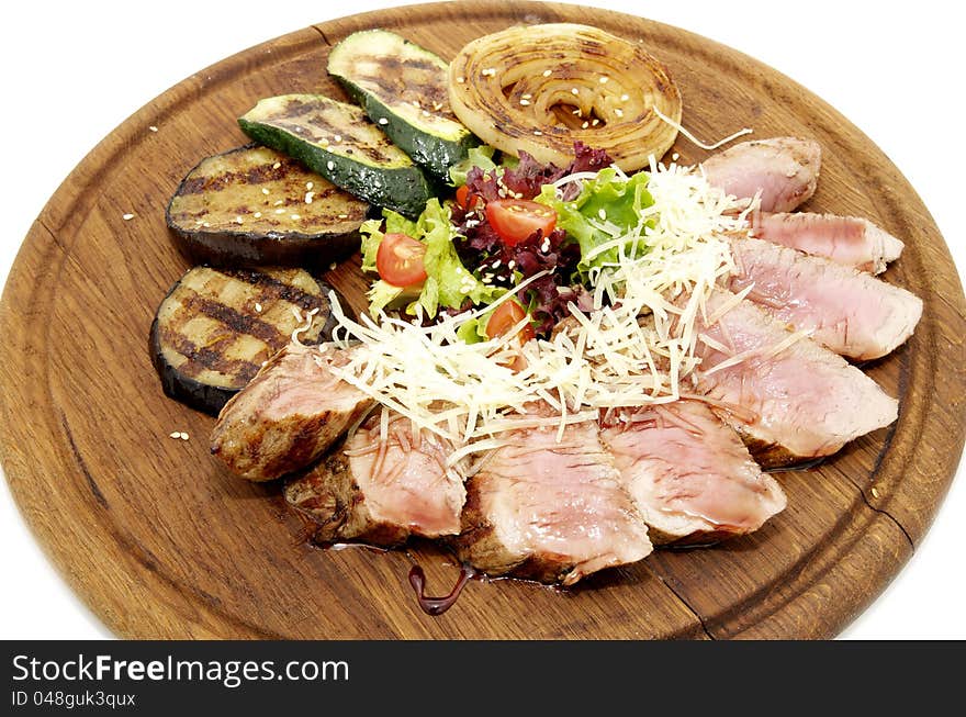 Meat roasted on a grill with vegetables on a wooden plate