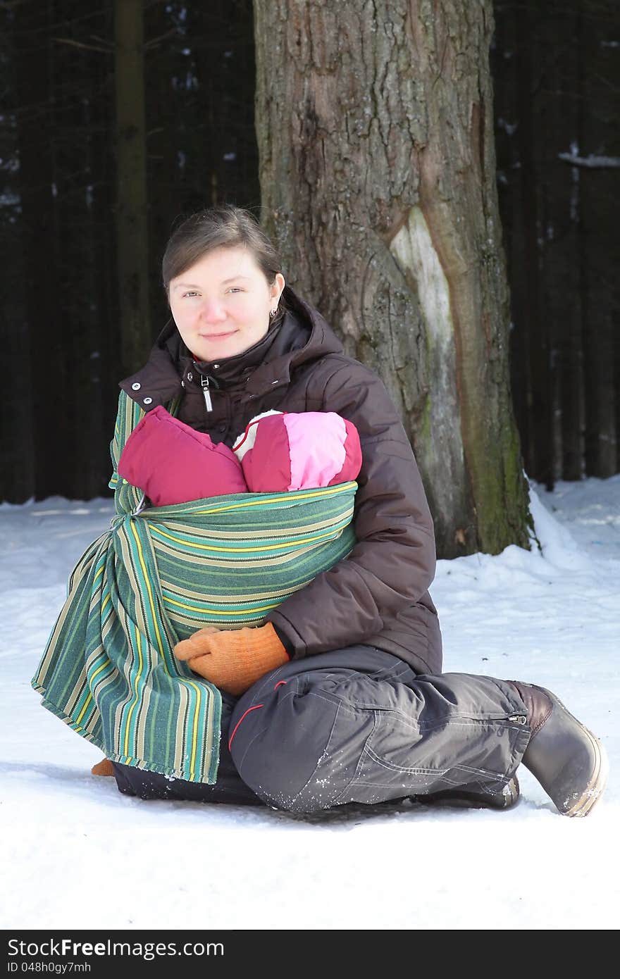 Sitting mother with newborn baby in the sling in winter