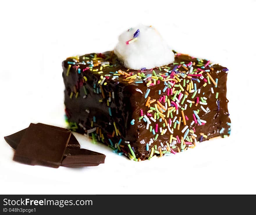 Chocolate cake with cream on top, multicolored sugar topping on sides and pieces of chocolate on the left on white background