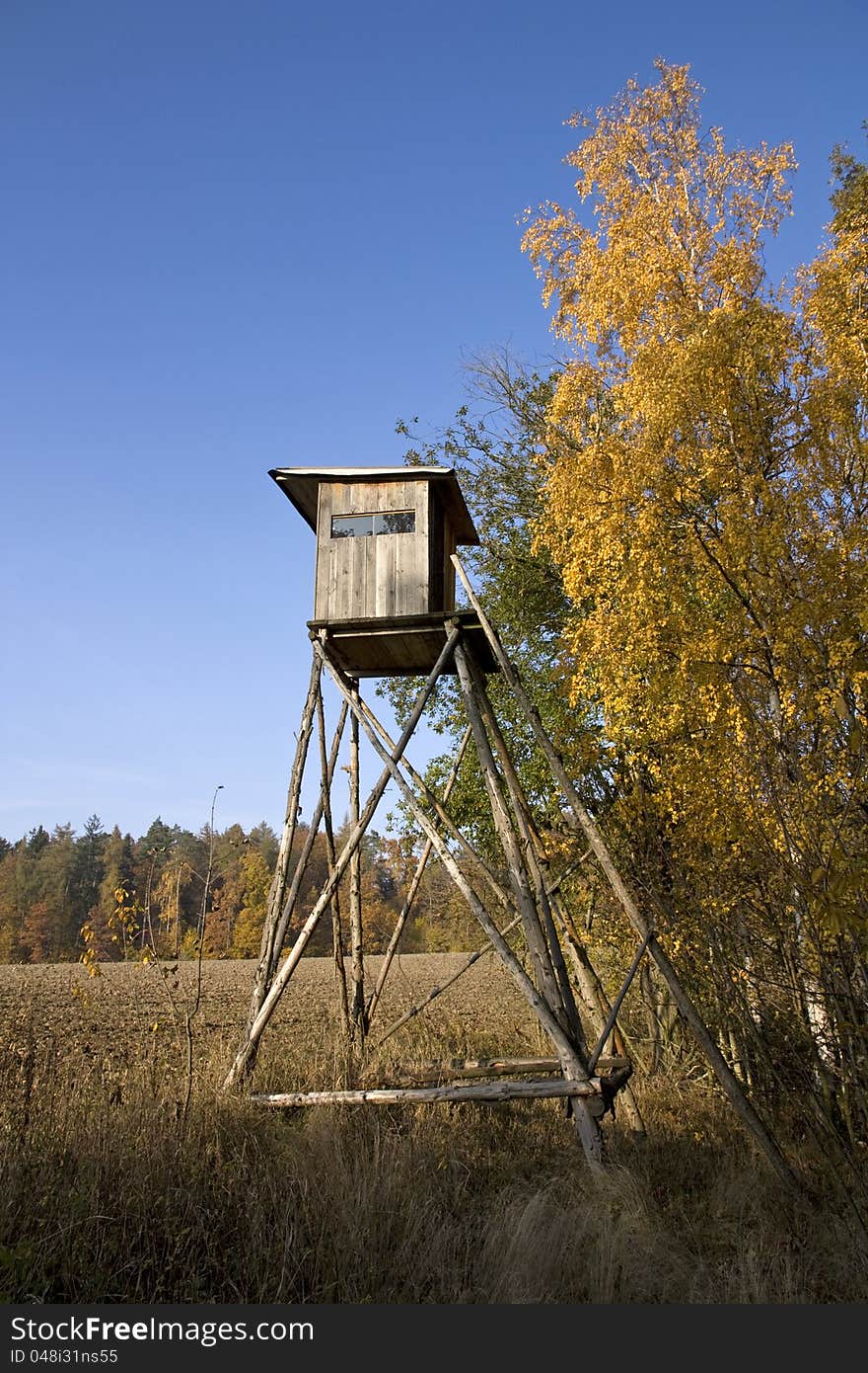 Wooden shelter for hunters, hunting shelter on the edge of the forest, with yellow birch leaves, autumn landscape with blue sky, brown plowed fields, forest land and fields. Wooden shelter for hunters, hunting shelter on the edge of the forest, with yellow birch leaves, autumn landscape with blue sky, brown plowed fields, forest land and fields