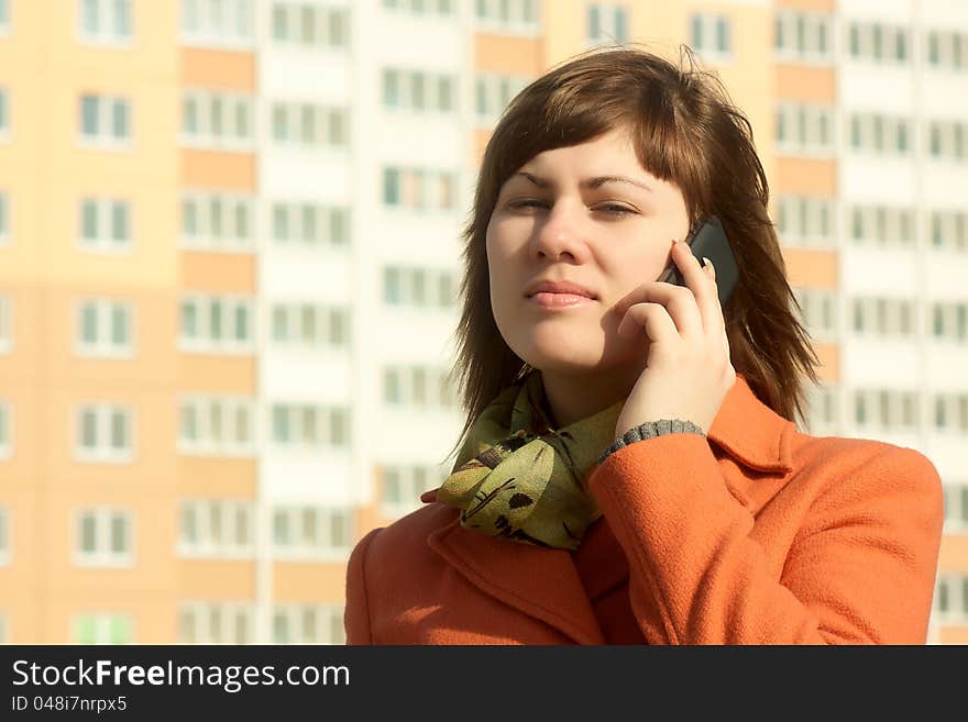 Woman orange coat make a call on modern background. Woman orange coat make a call on modern background