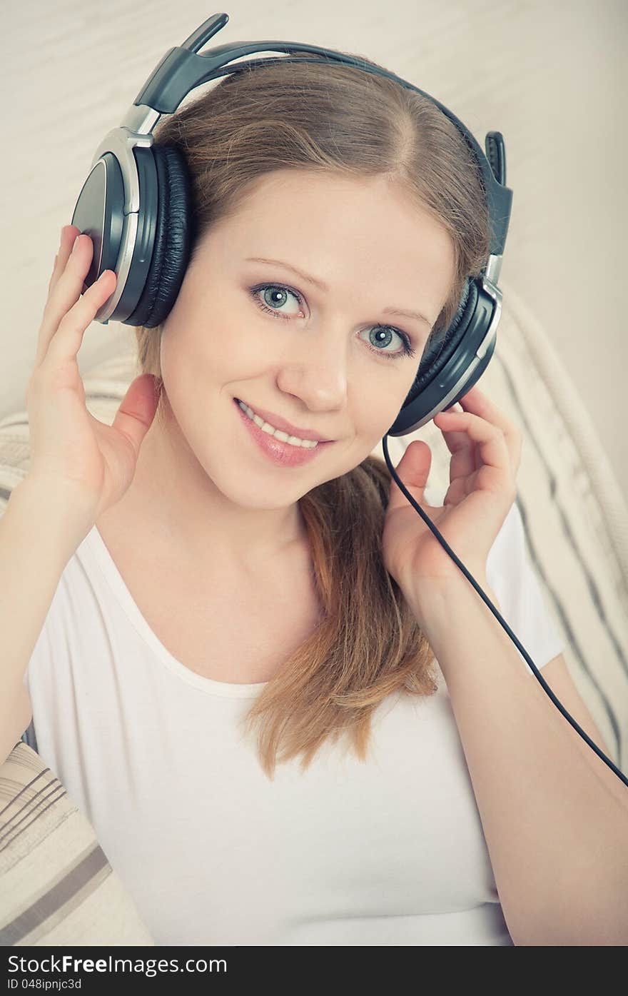 Beautiful young woman enjoys listening to music on headphones while lying on the sofa