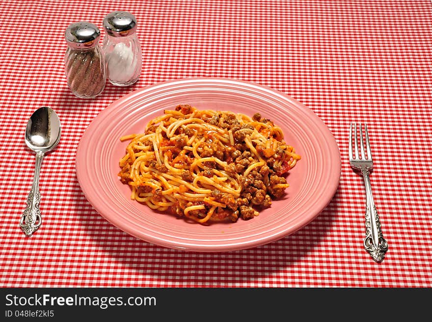 A plate full of spaghetti on a red check table cloth