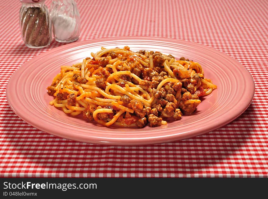 A plate full of spaghetti on a red check table cloth