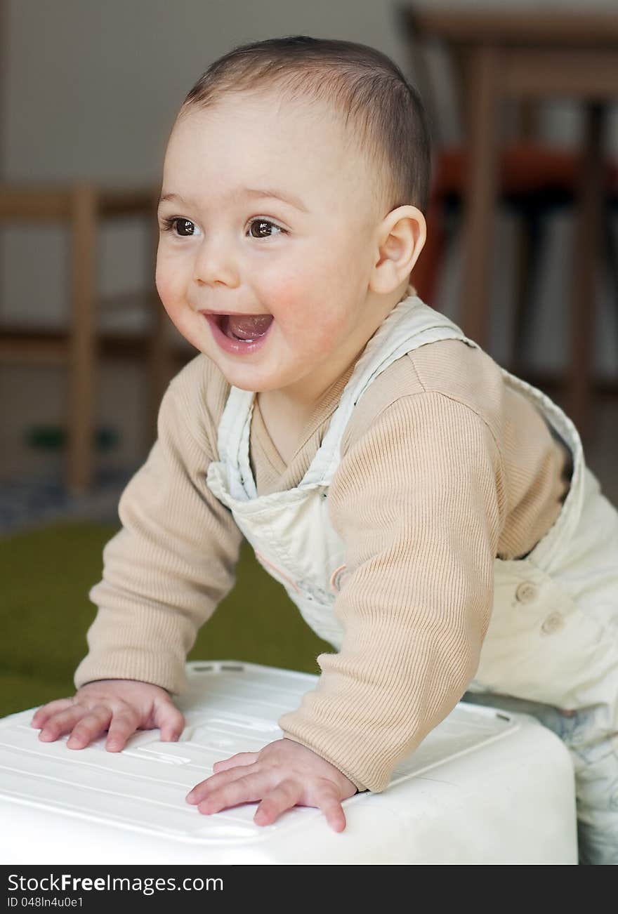 Portrait of a cute happy smiling 7 month old baby, boy or girl, standing leaning against a stool.