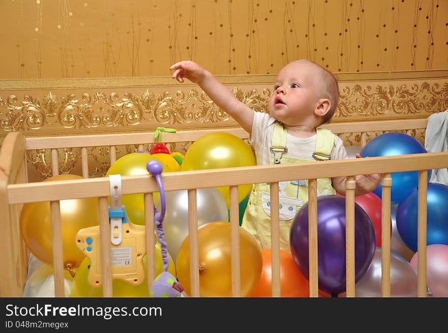 The child in a bed with balloons of different color against wall-paper