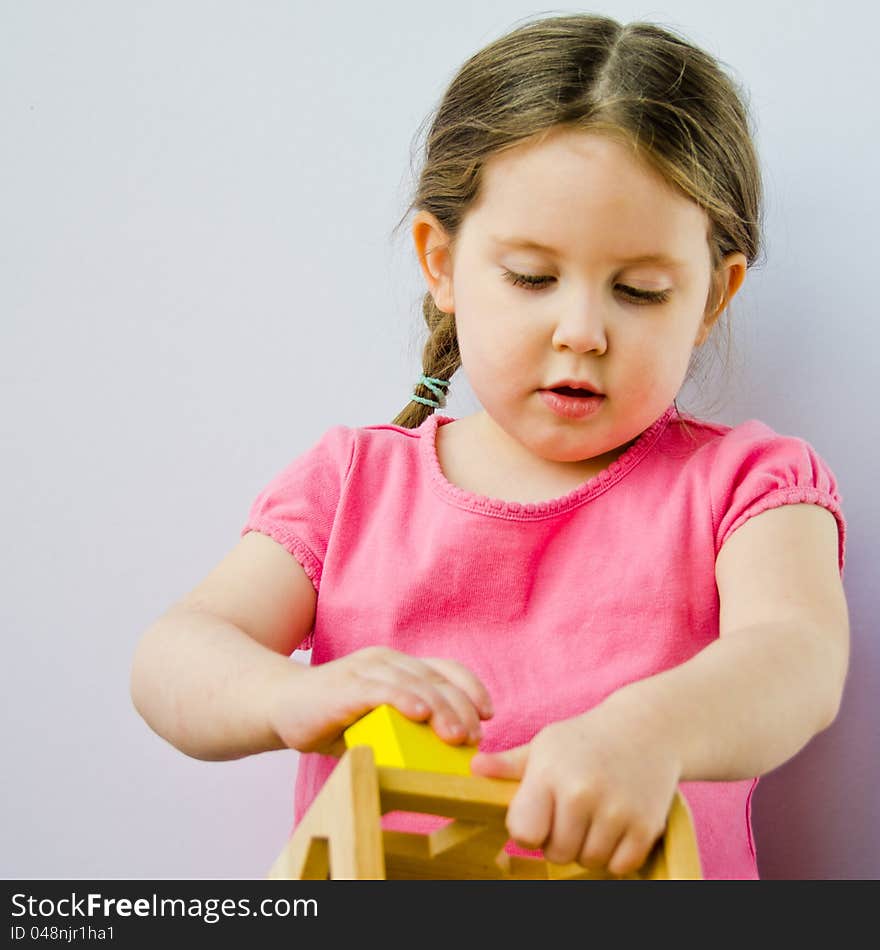 A three-year-old girl with pigtails on white plays with block puzzlle. A three-year-old girl with pigtails on white plays with block puzzlle