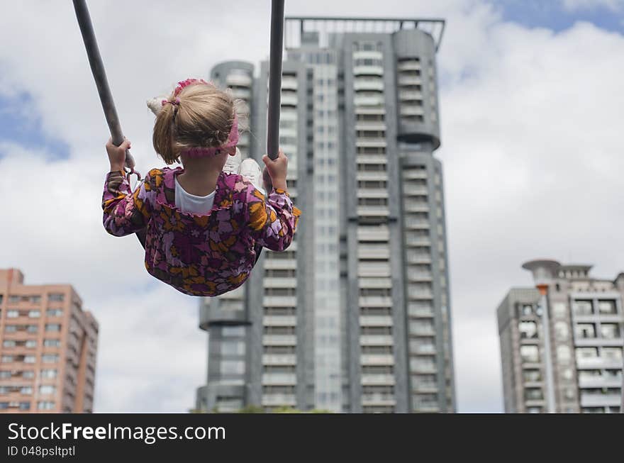 Little girl swinging with buildings in the background. Little girl swinging with buildings in the background