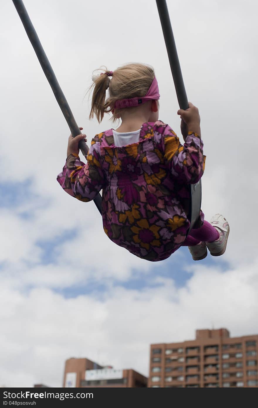 Little girl swinging with buildings in the background. Little girl swinging with buildings in the background