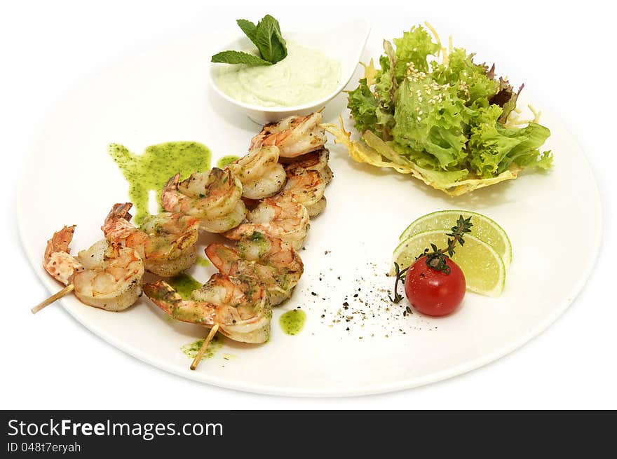 Skewers of shrimp on a white plate with vegetables and lemon