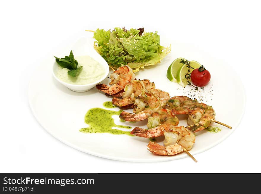 Skewers of shrimp on a white plate with vegetables and lemon