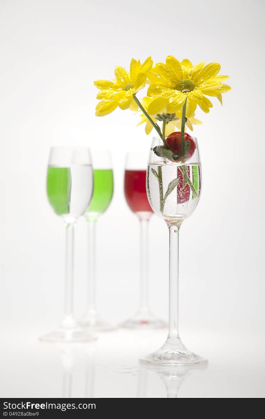 A glass, cherry and yellow flowers on a white background. Flowers in the water.