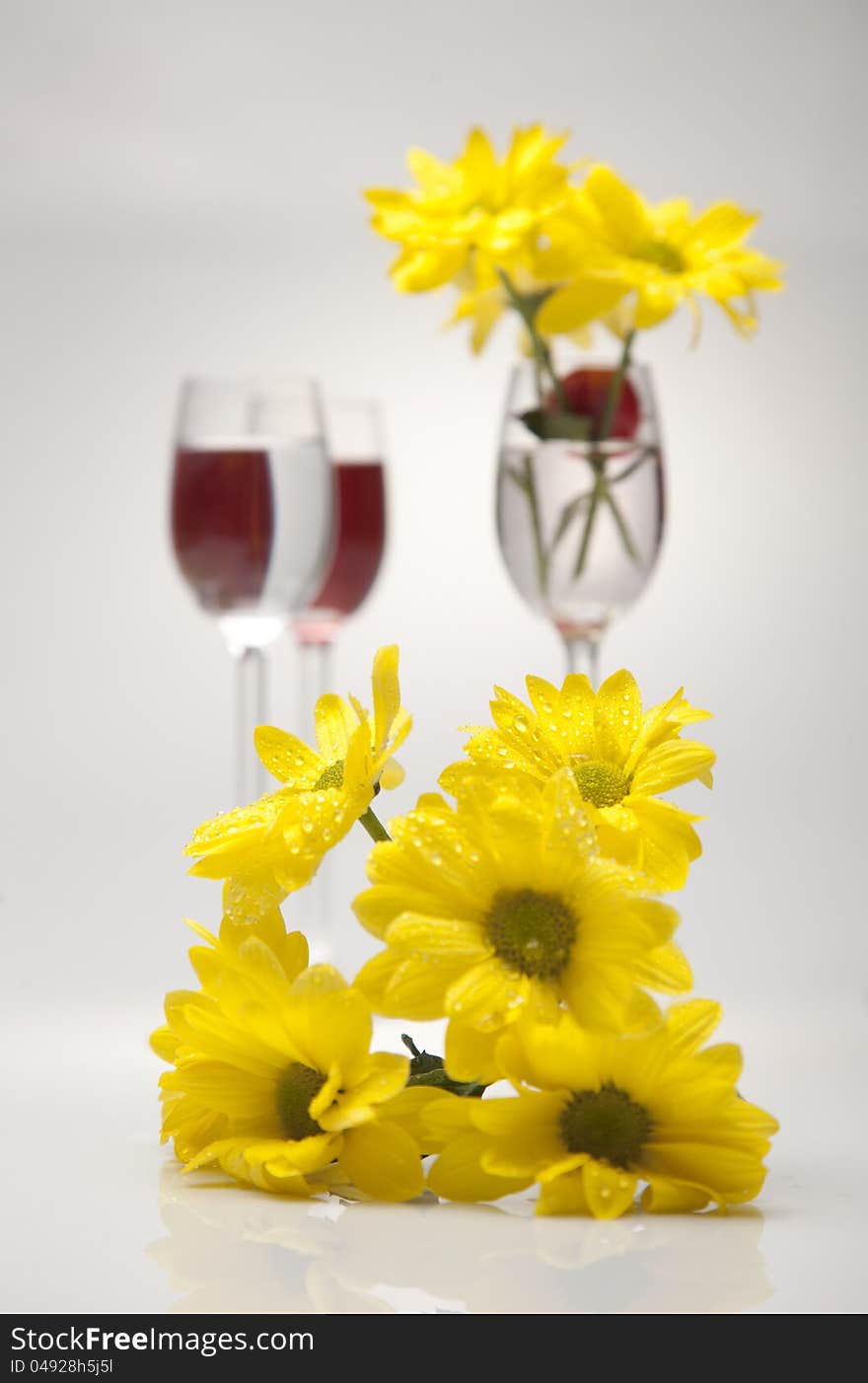 A Glass, Cherry And Yellow Flowers On A White Back