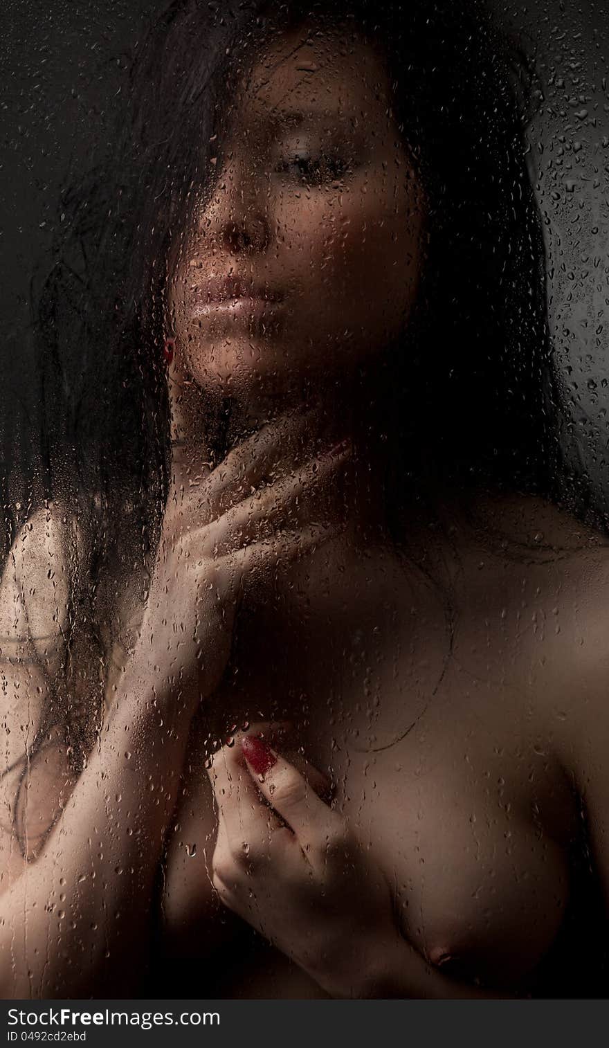 Naked girl in a wet glass on a white background. She has a sad face.