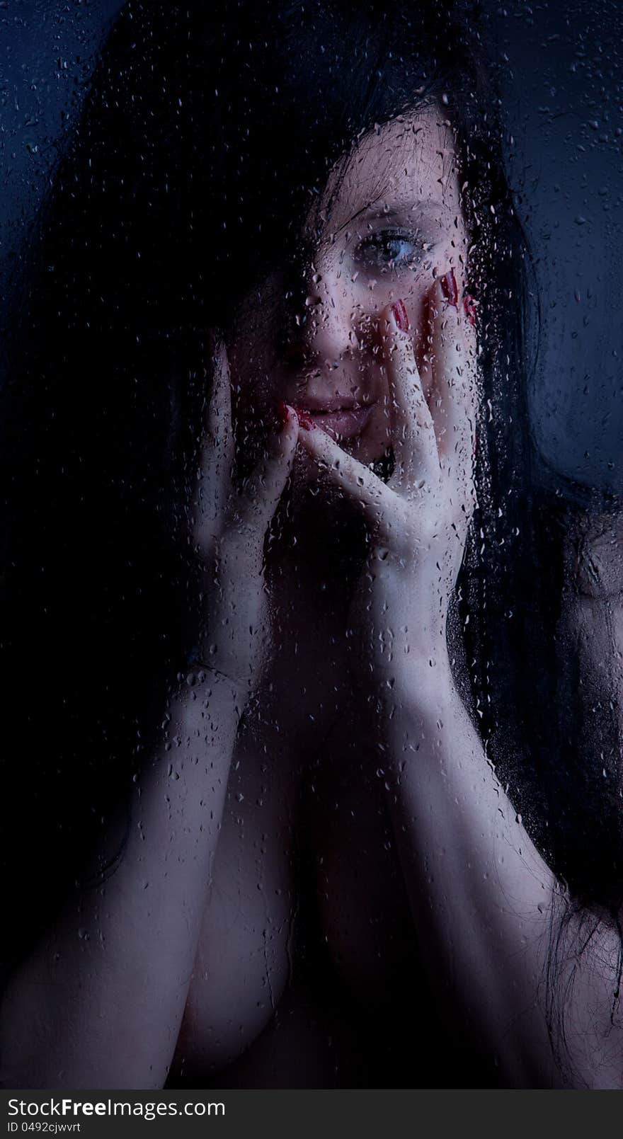 Naked girl in a wet glass on a white background. She has a sad face.