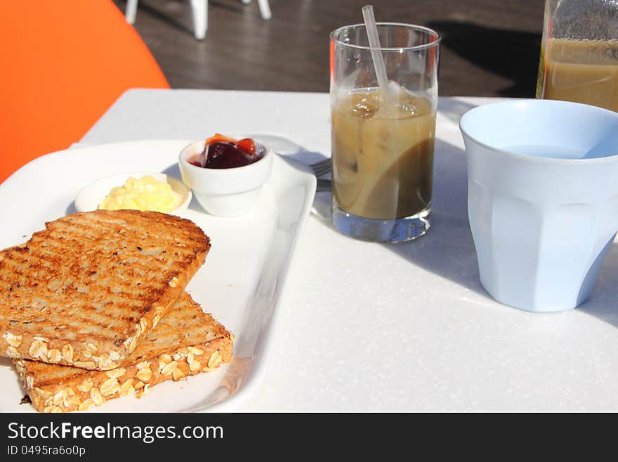 A simple breakfast served at a cafe: two wholemeal toasts with butter and raspberry jam, a cup of tap water and a healthy green juice. A simple breakfast served at a cafe: two wholemeal toasts with butter and raspberry jam, a cup of tap water and a healthy green juice