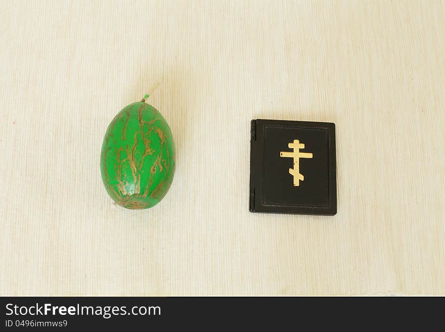 Candle in the form of Easter egg green close-up on the table next to the image of an Orthodox cross. Candle in the form of Easter egg green close-up on the table next to the image of an Orthodox cross.