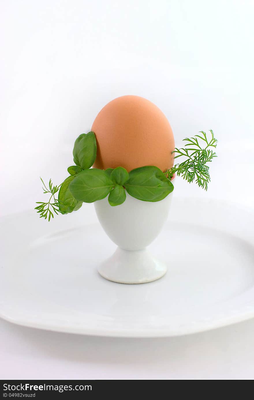 Egg in eggcup on the white plate, decorated with greenery