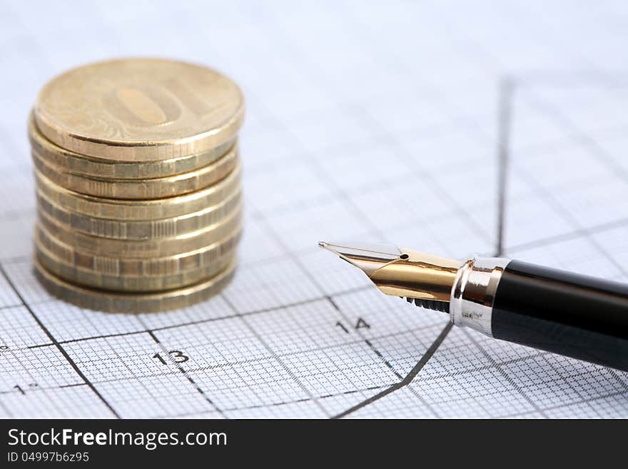 Business concept. Closeup of fountain pen near stack of coins on graph paper with diagram. Business concept. Closeup of fountain pen near stack of coins on graph paper with diagram