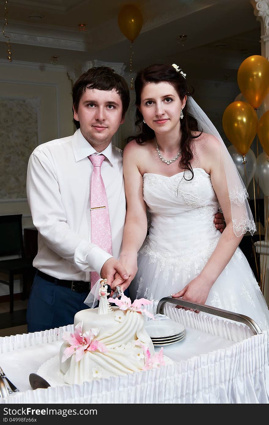 Bride and groom cuts the wedding cake with pink flowers