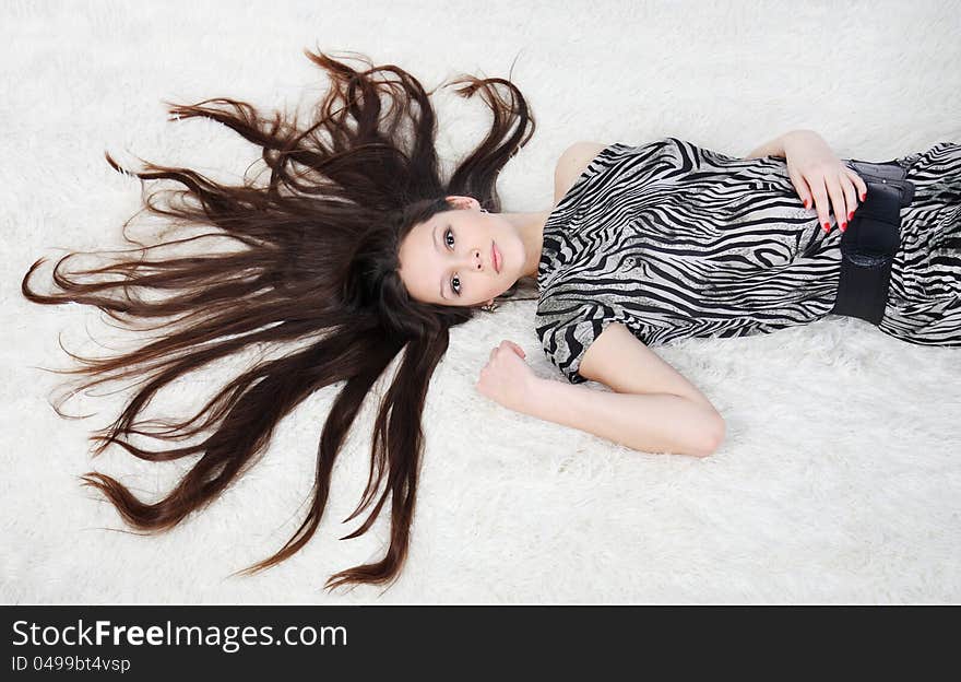 Beautiful girl with long hair wearing striped dress lies on white fur in studio. Beautiful girl with long hair wearing striped dress lies on white fur in studio