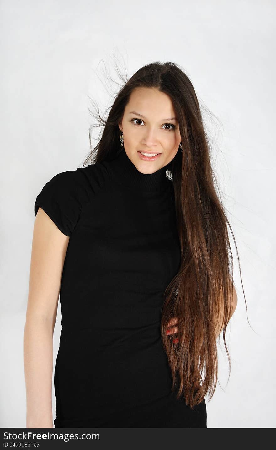 Beautiful brunette girl wearing black dress looks at camera and smiles in white studio