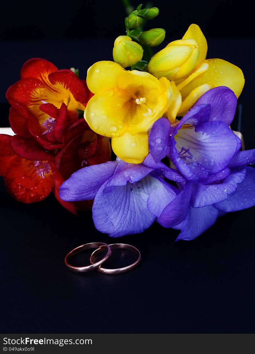 Wedding rings and a bouquet of freesias on a black background