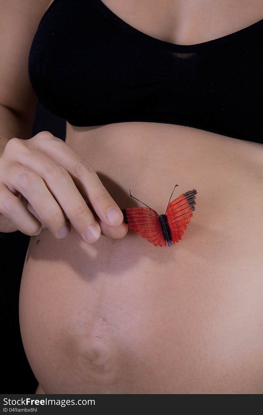 Hand of a pregnant woman holding a red butterfly on her tummy. Hand of a pregnant woman holding a red butterfly on her tummy