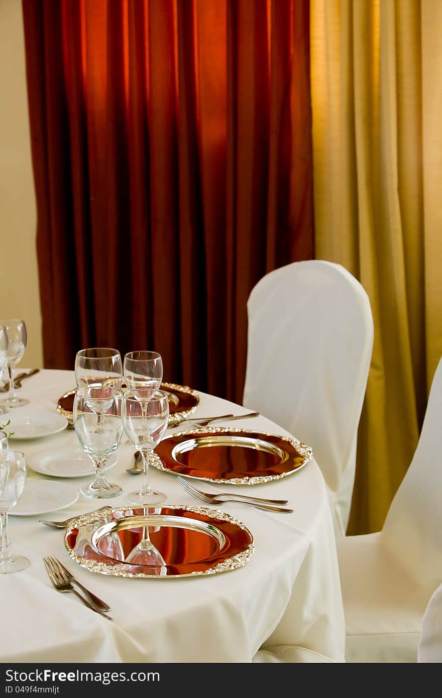 Wedding table and chairs with white tableclothes and silver platters set for fine dining. Wedding table and chairs with white tableclothes and silver platters set for fine dining