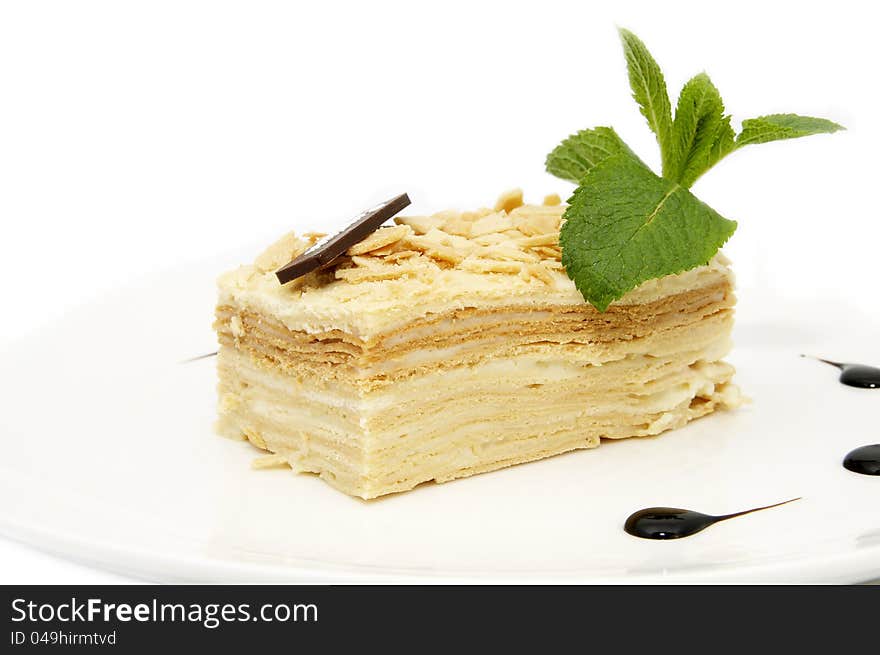 Piece of layer cake decorated with a mint on a white plate. Piece of layer cake decorated with a mint on a white plate