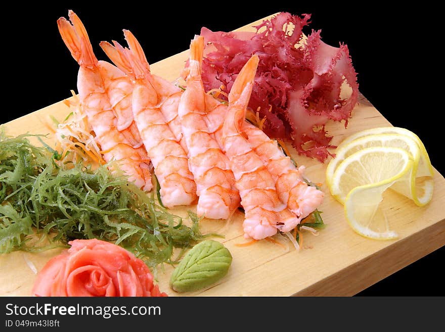 Sashimi eb with shrimps, lemon lobules, ginger, wasabi, red and green algae on rectangular board isolated on a black background. Sashimi eb with shrimps, lemon lobules, ginger, wasabi, red and green algae on rectangular board isolated on a black background