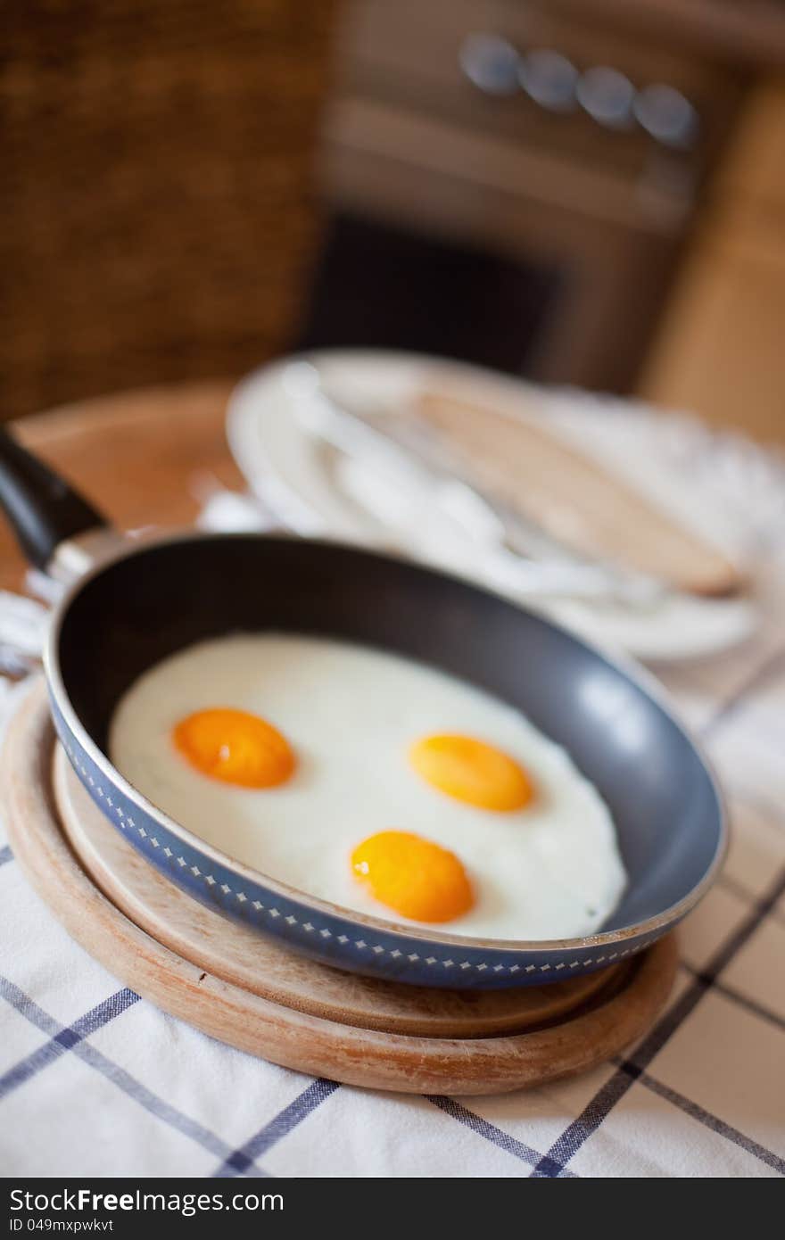 Picture of three fried eggs in a pan, standing on a kitchen table