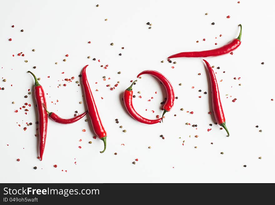 Red chili peppers shaping the word hot, surrounded with peppercorns, isolated on white background. Red chili peppers shaping the word hot, surrounded with peppercorns, isolated on white background