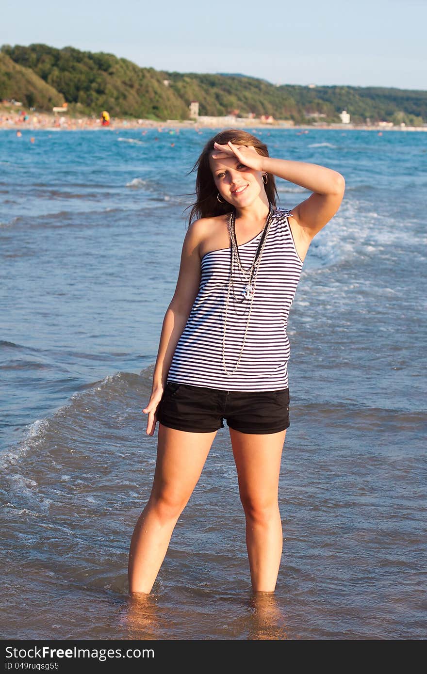 Young pretty girl looking at camers and smiling with the sea as a background. Young pretty girl looking at camers and smiling with the sea as a background