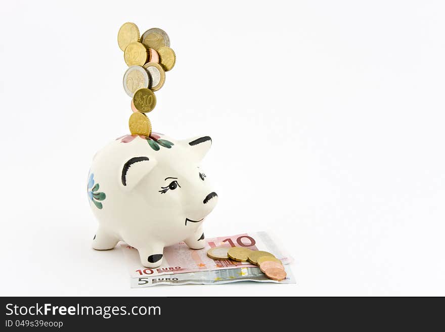 Coins falling into a piggy bank, which is depicted on banknotes, coins, on which lie on a white background.