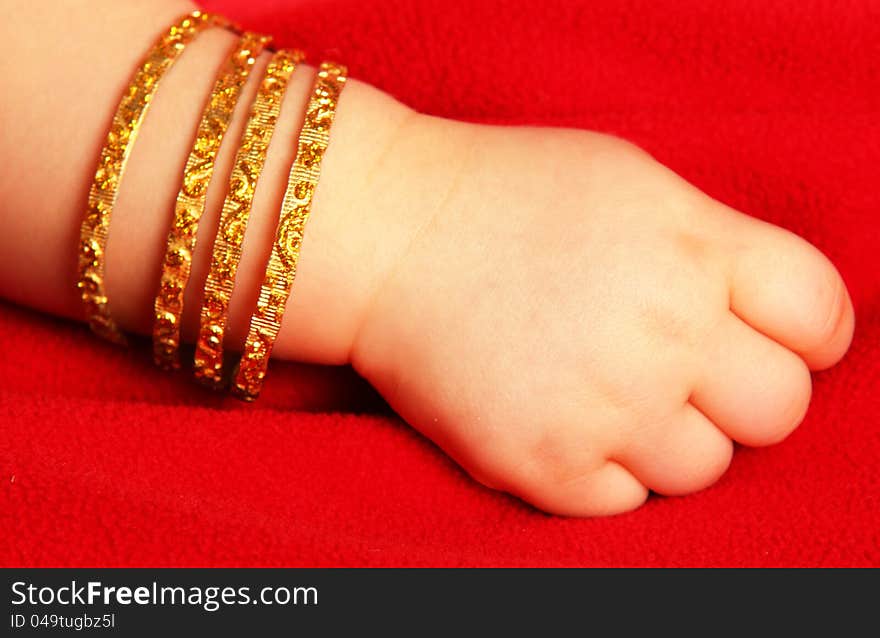 Baby hand, with golden bracelets, towards dark red